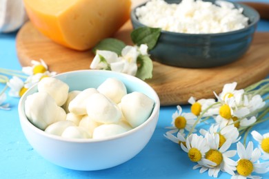 Photo of Different fresh dairy products and flowers on light blue wooden table, closeup
