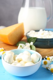Photo of Different fresh dairy products and flowers on light blue wooden table, closeup