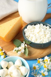 Photo of Different fresh dairy products and flowers on light blue wooden table, closeup