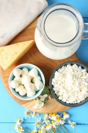 Photo of Different fresh dairy products and flowers on light blue wooden table, flat lay