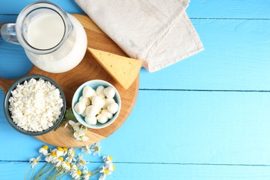 Photo of Different fresh dairy products and flowers on light blue wooden table, flat lay. Space for text