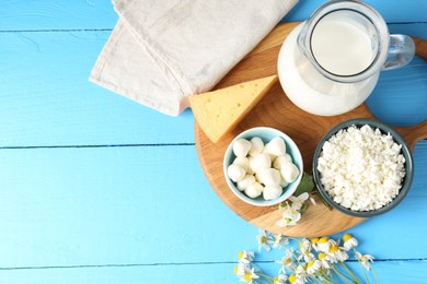 Photo of Different fresh dairy products and flowers on light blue wooden table, flat lay. Space for text