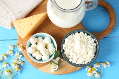 Photo of Different fresh dairy products and flowers on light blue wooden table, flat lay