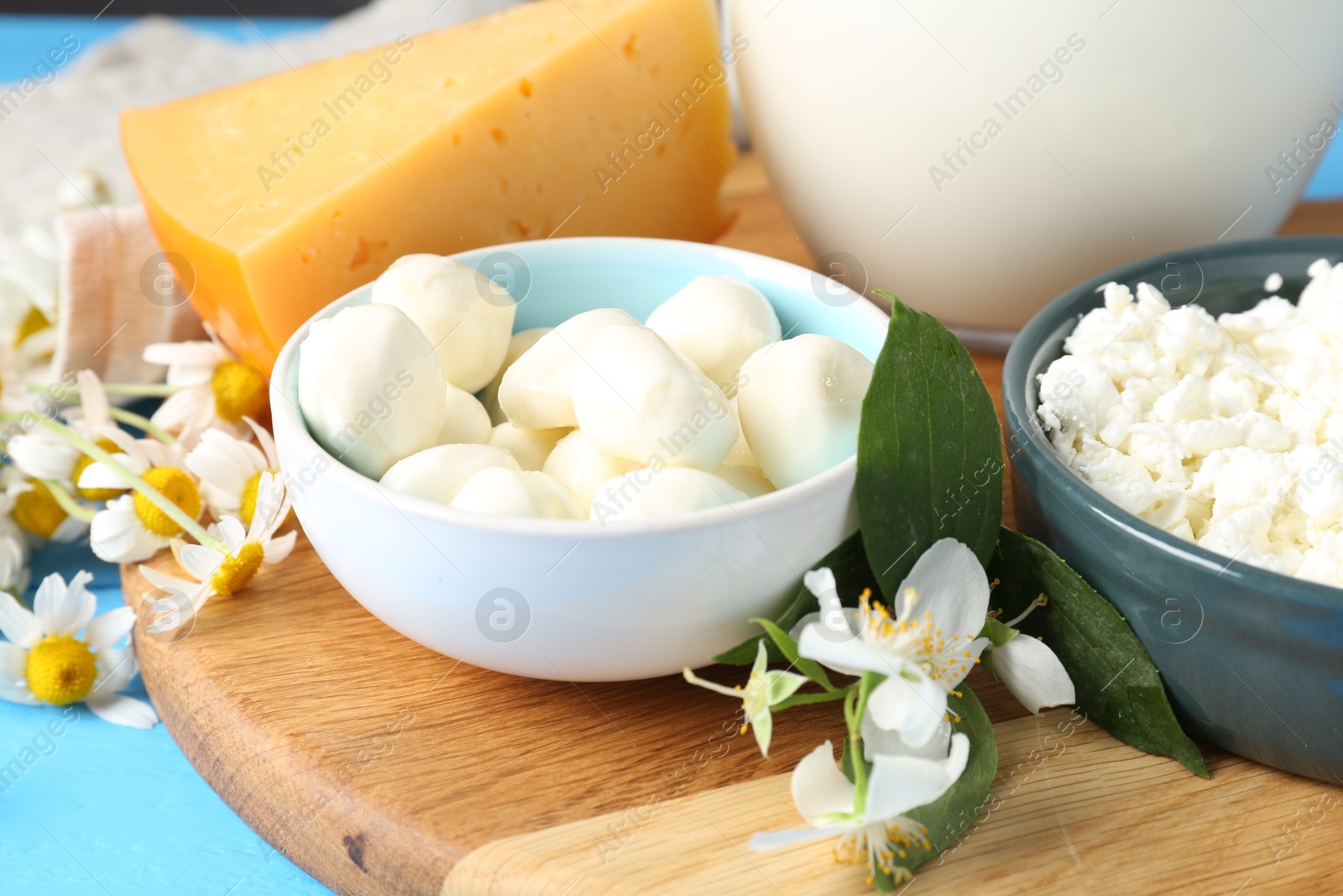 Photo of Different fresh dairy products and flowers on light blue table, closeup