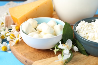Photo of Different fresh dairy products and flowers on light blue table, closeup