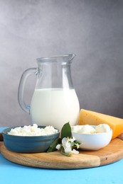 Photo of Different fresh dairy products and flowers on light blue wooden table, closeup