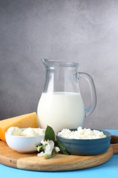 Photo of Different fresh dairy products and flowers on light blue wooden table, closeup