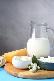 Photo of Different fresh dairy products and flowers on light blue wooden table, closeup