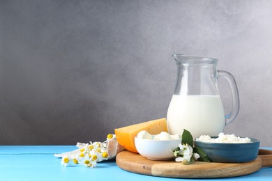 Photo of Different fresh dairy products and flowers on light blue wooden table, space for text
