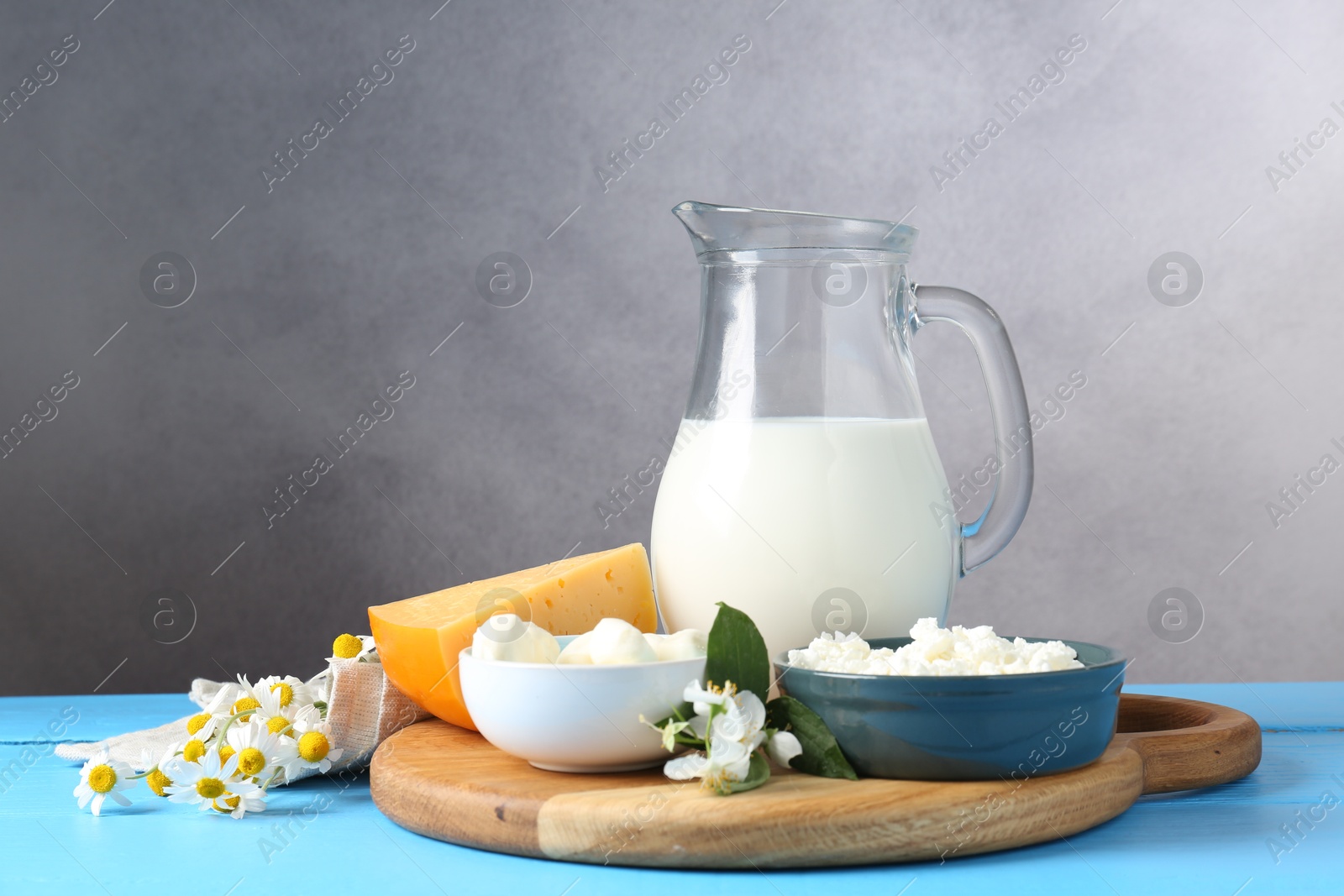 Photo of Different fresh dairy products and flowers on light blue wooden table