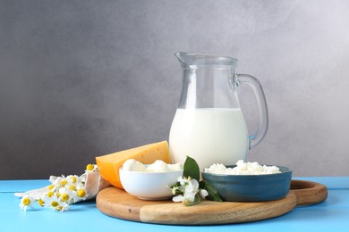 Photo of Different fresh dairy products and flowers on light blue wooden table