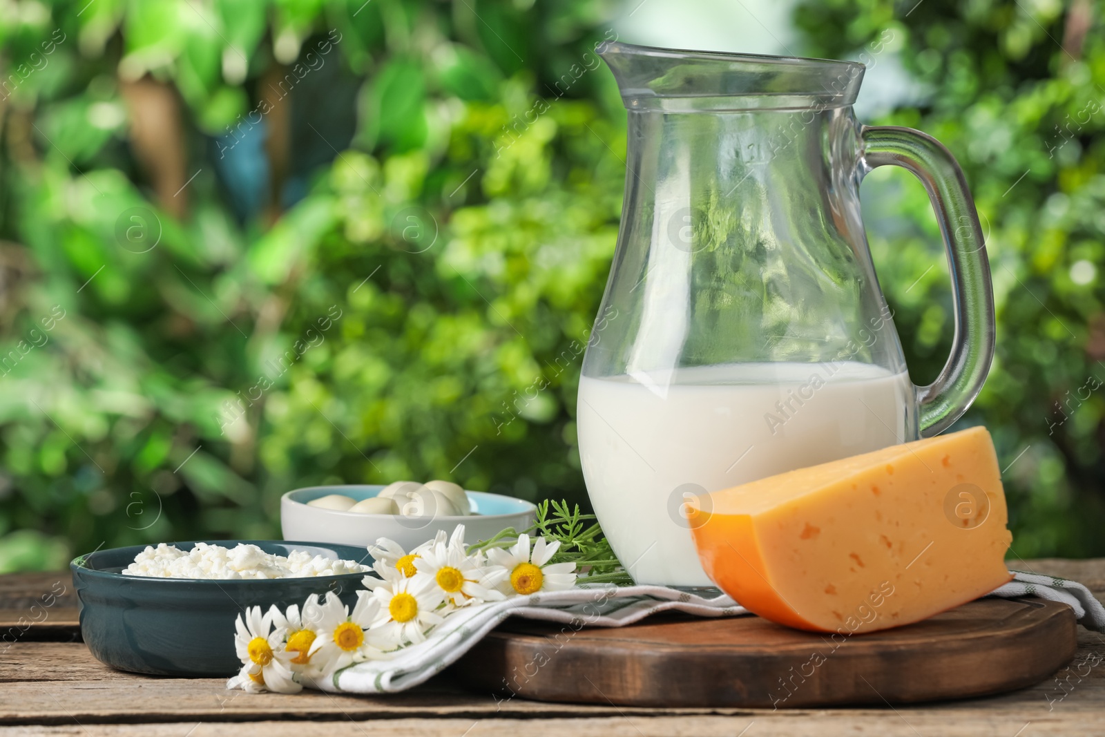 Photo of Different fresh dairy products and flowers on wooden table outdoors