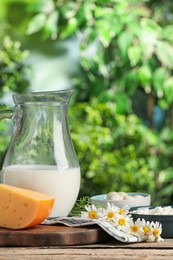 Photo of Different fresh dairy products and flowers on wooden table outdoors