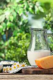 Photo of Different fresh dairy products and flowers on wooden table outdoors