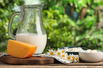 Photo of Different fresh dairy products and flowers on wooden table outdoors