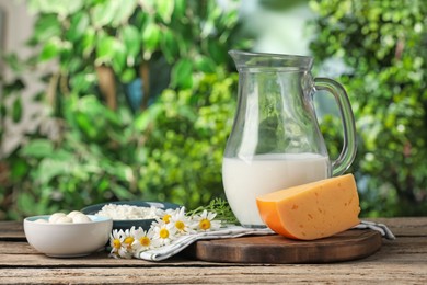 Photo of Different fresh dairy products and flowers on wooden table outdoors