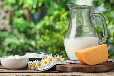 Photo of Different fresh dairy products and flowers on wooden table outdoors, closeup