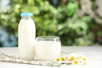 Photo of Fresh milk in glass, bottle and chamomile flowers on white wooden table outdoors, space for text. Dairy product