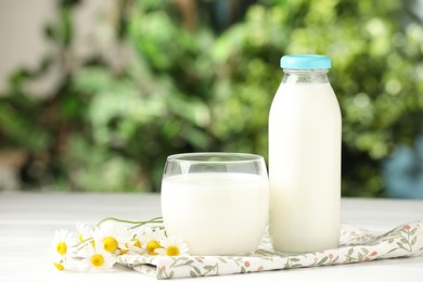 Photo of Fresh milk in glass, bottle and chamomile flowers on white wooden table outdoors. Dairy product