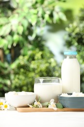 Photo of Different fresh dairy products and flowers on white table outdoors