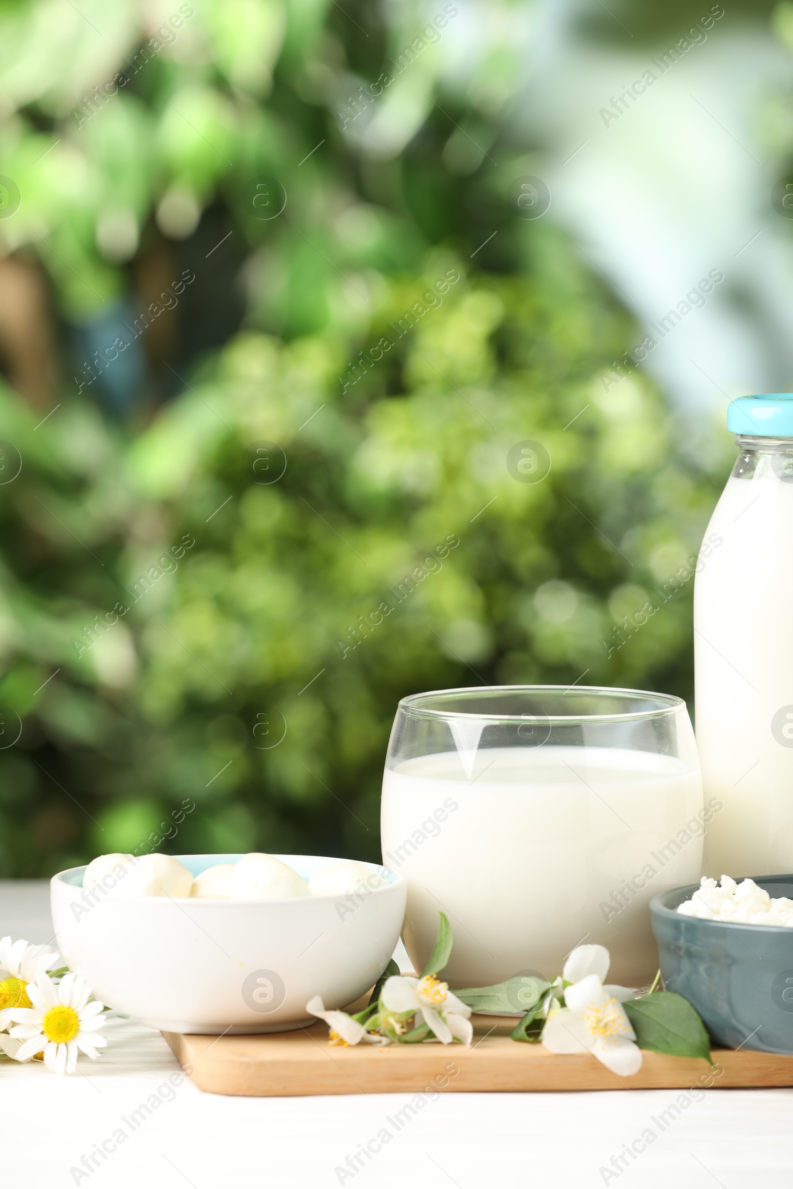 Photo of Different fresh dairy products and flowers on white table outdoors, closeup