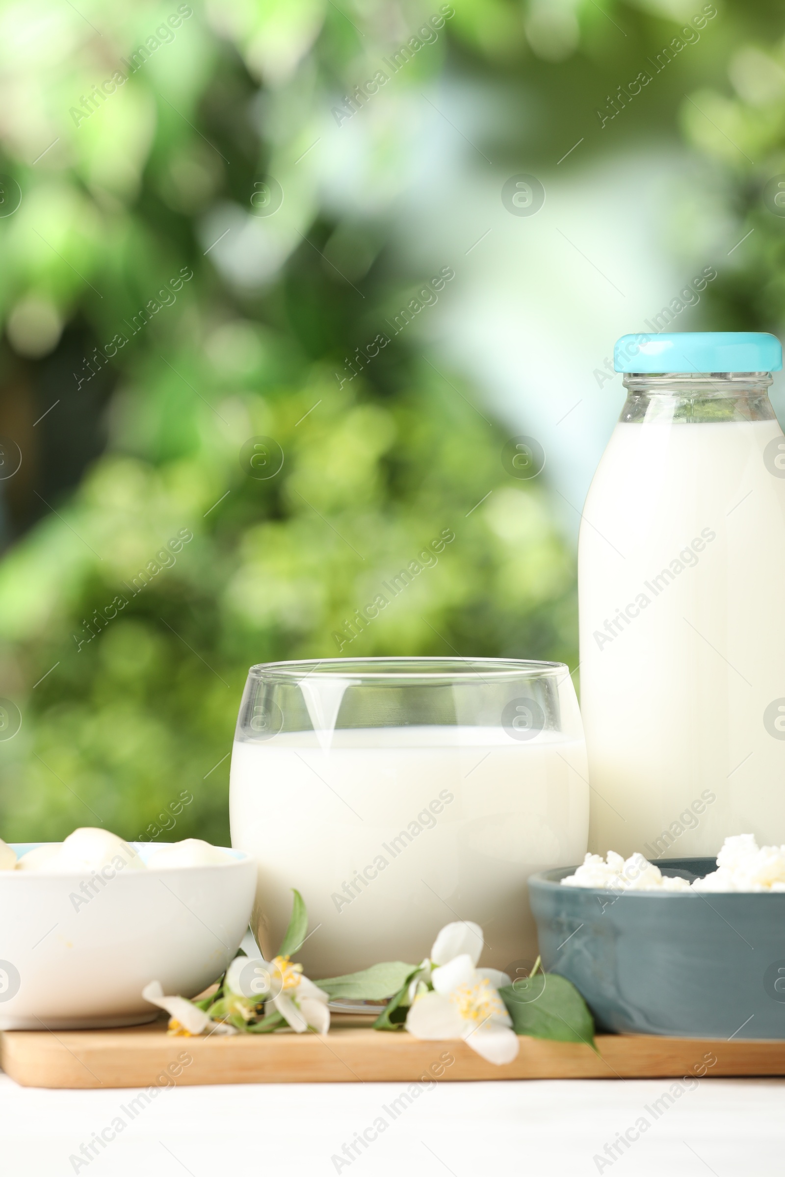 Photo of Different fresh dairy products and flowers on white table outdoors, closeup