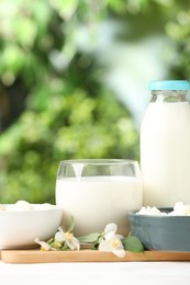 Photo of Different fresh dairy products and flowers on white table outdoors, closeup