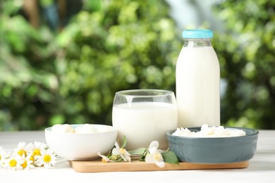 Photo of Different fresh dairy products and flowers on white wooden table outdoors