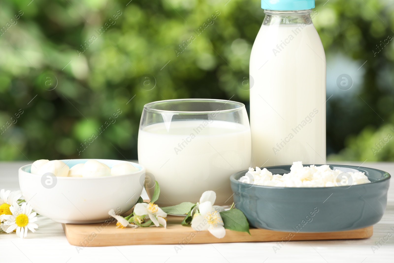 Photo of Different fresh dairy products and flowers on white wooden table outdoors, closeup