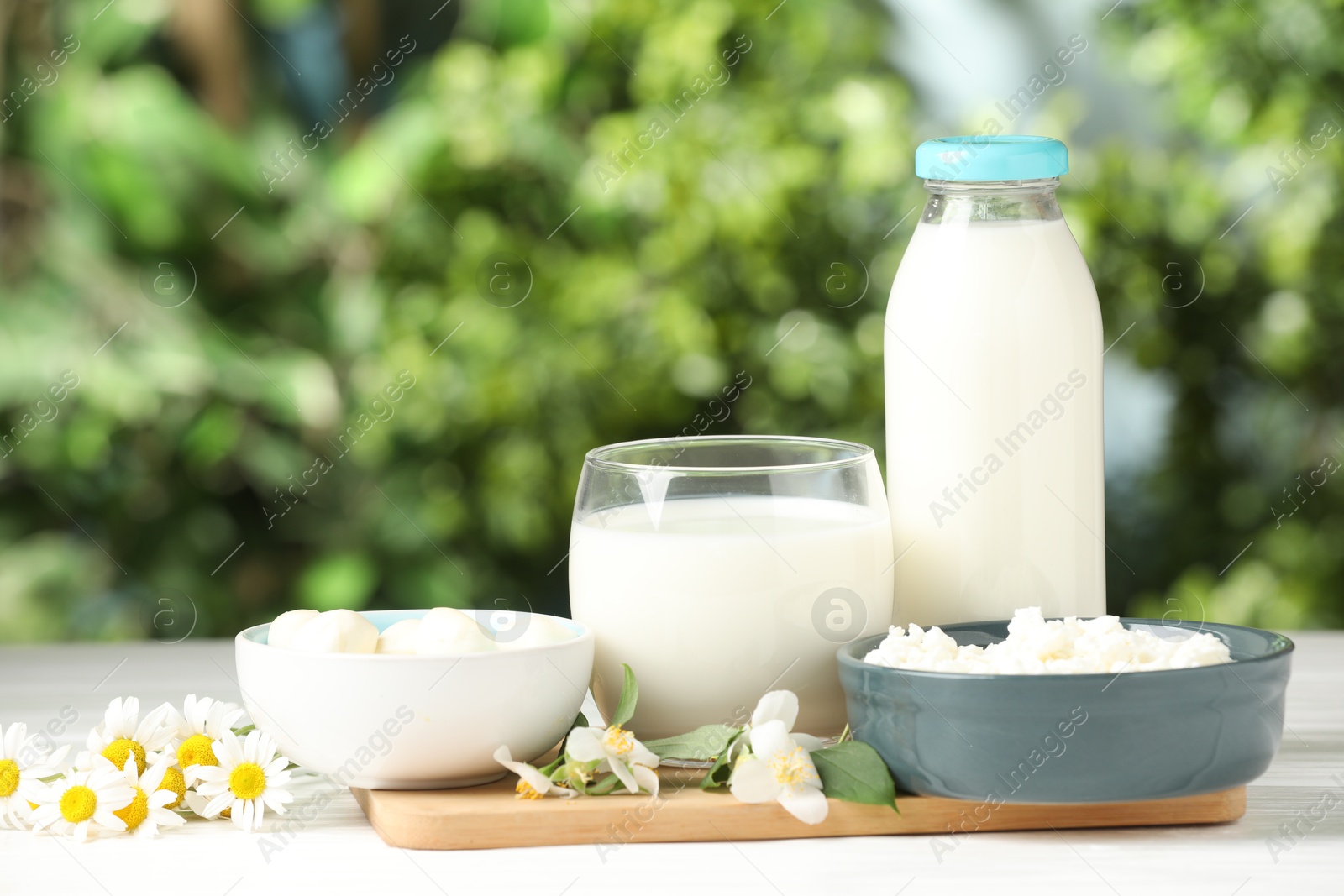 Photo of Different fresh dairy products and flowers on white wooden table outdoors
