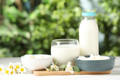 Photo of Different fresh dairy products and flowers on white wooden table outdoors