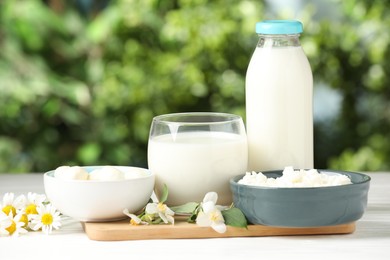 Photo of Different fresh dairy products and flowers on white wooden table outdoors