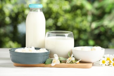 Photo of Different fresh dairy products and flowers on white wooden table outdoors
