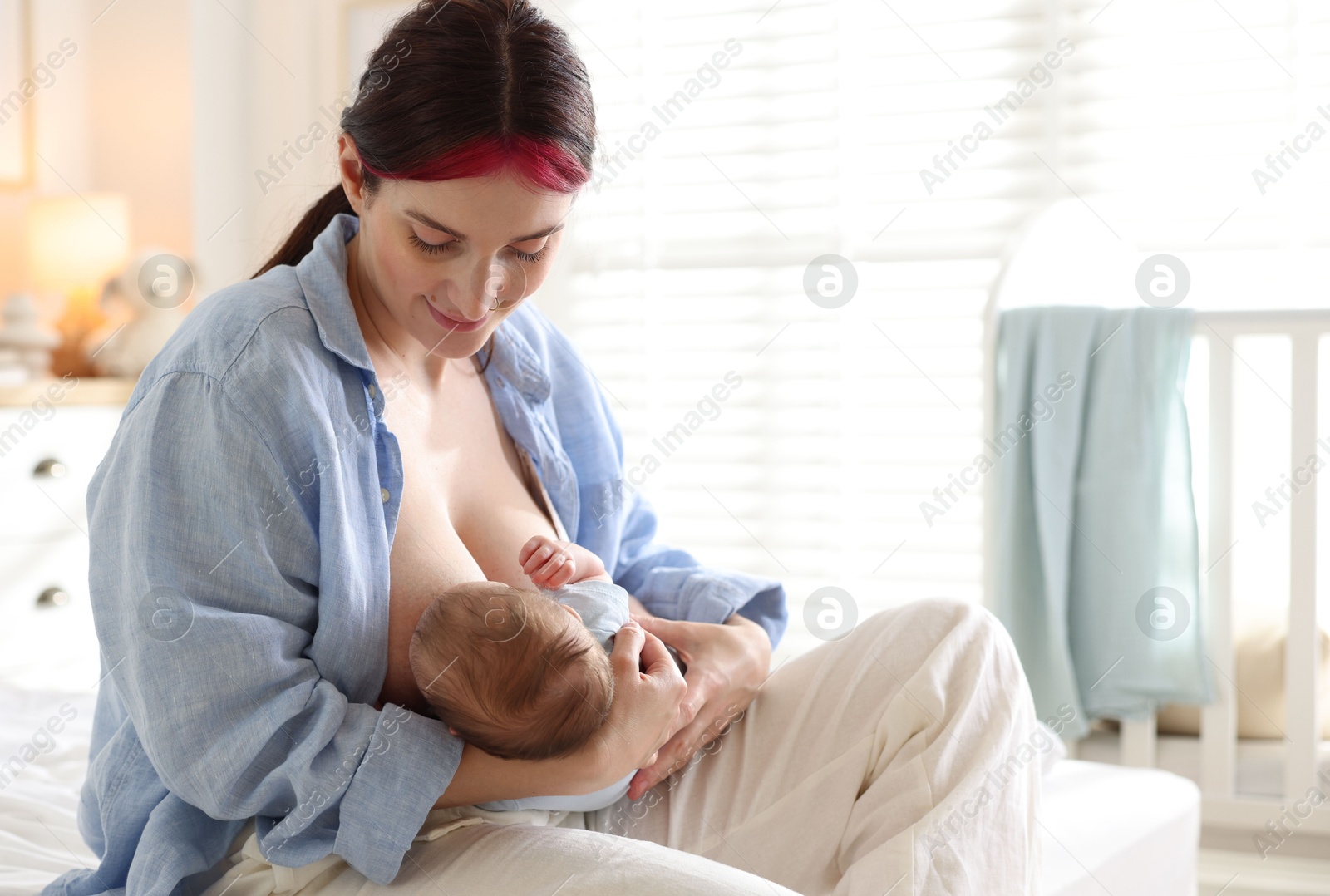 Mother breastfeeding her newborn baby on bed indoors Photo of Mother breastfeeding her newborn baby on bed indoors