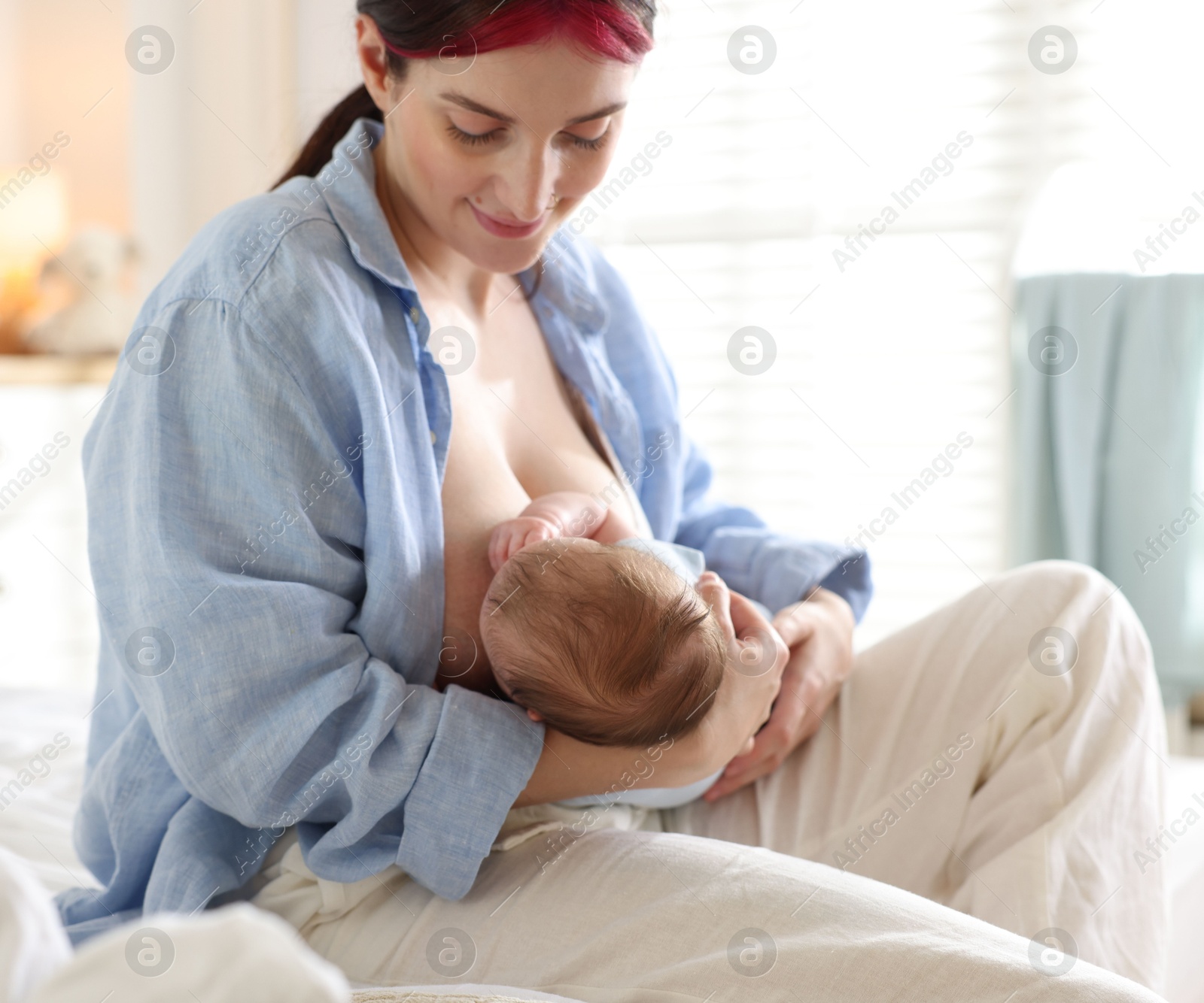 Mother breastfeeding her newborn baby on bed indoors Photo of Mother breastfeeding her newborn baby on bed indoors