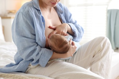 Photo of Mother breastfeeding her newborn baby on bed indoors, closeup