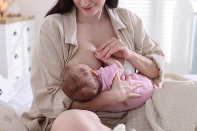 Photo of Mother breastfeeding her newborn baby on bed indoors, closeup