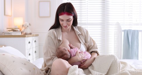Photo of Mother breastfeeding her newborn baby on bed indoors