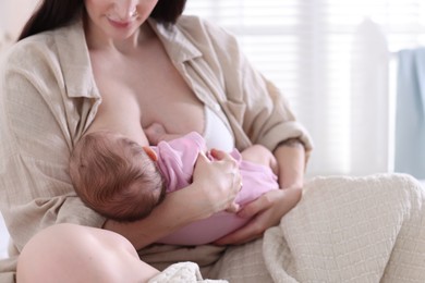 Photo of Mother breastfeeding her newborn baby on bed indoors, closeup