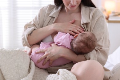 Photo of Mother breastfeeding her newborn baby on bed indoors, closeup