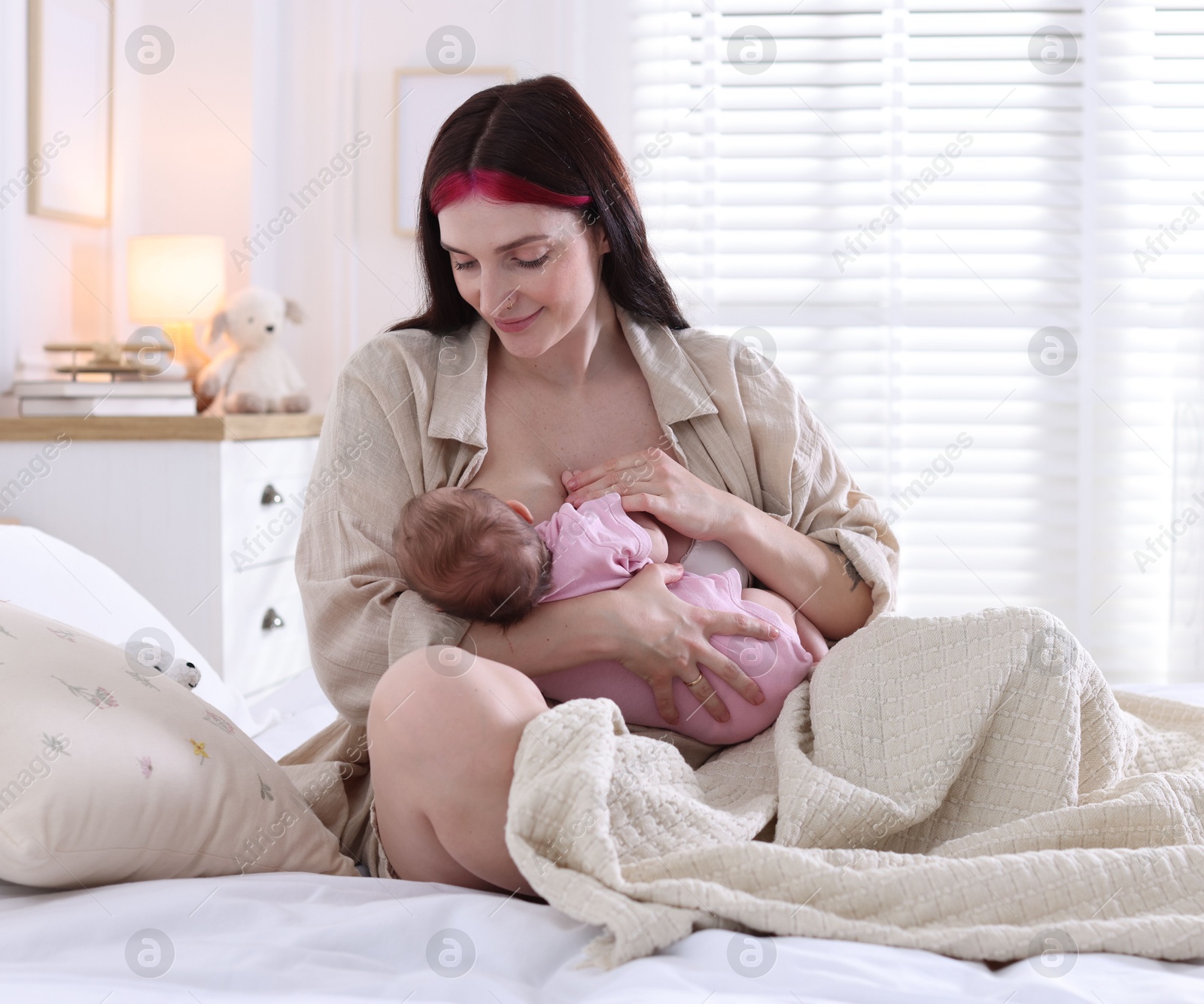 Mother breastfeeding her newborn baby on bed indoors Photo of Mother breastfeeding her newborn baby on bed indoors