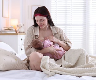 Photo of Mother breastfeeding her newborn baby on bed indoors