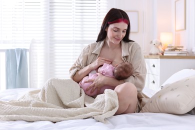 Photo of Mother breastfeeding her newborn baby on bed indoors