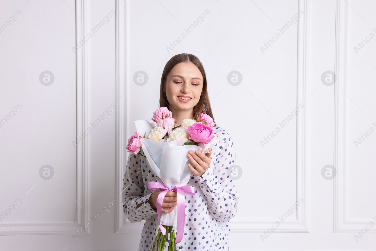 Woman with beautiful bouquet of peonies near white wall indoors Photo of Woman with beautiful bouquet of peonies near white wall indoors