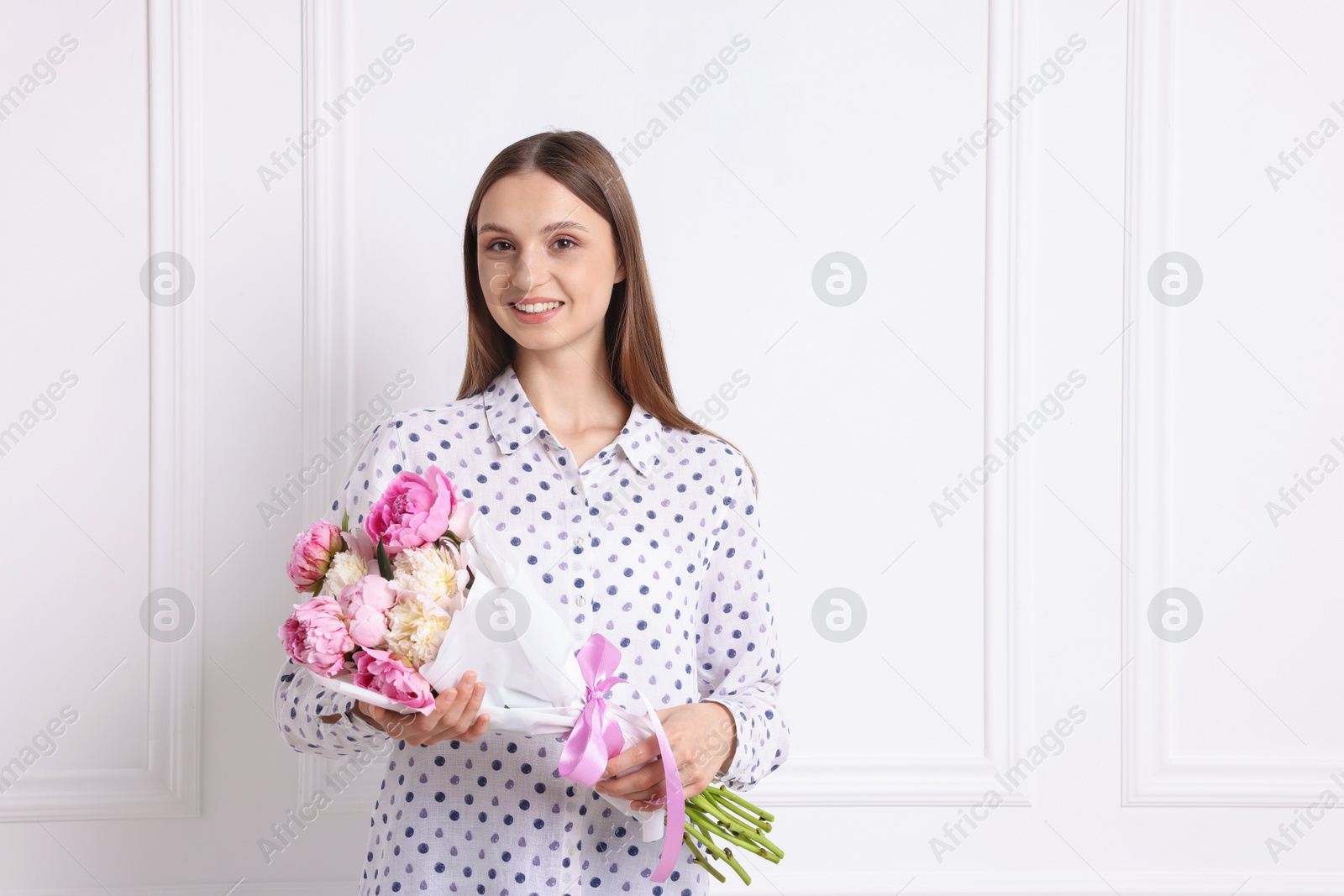 Woman with beautiful bouquet of peonies near white wall indoors, space for text Photo of Woman with beautiful bouquet of peonies near white wall indoors, space for text