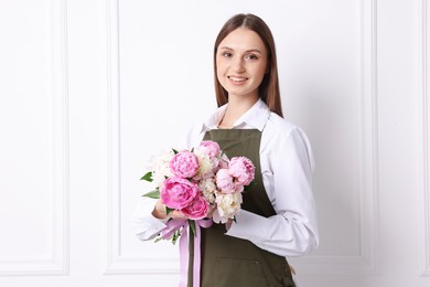 Photo of Florist with beautiful bouquet of peonies near white wall indoors