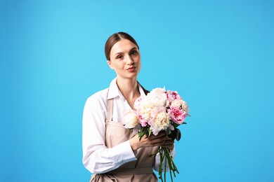 Photo of Florist with beautiful bouquet of peonies on light blue background