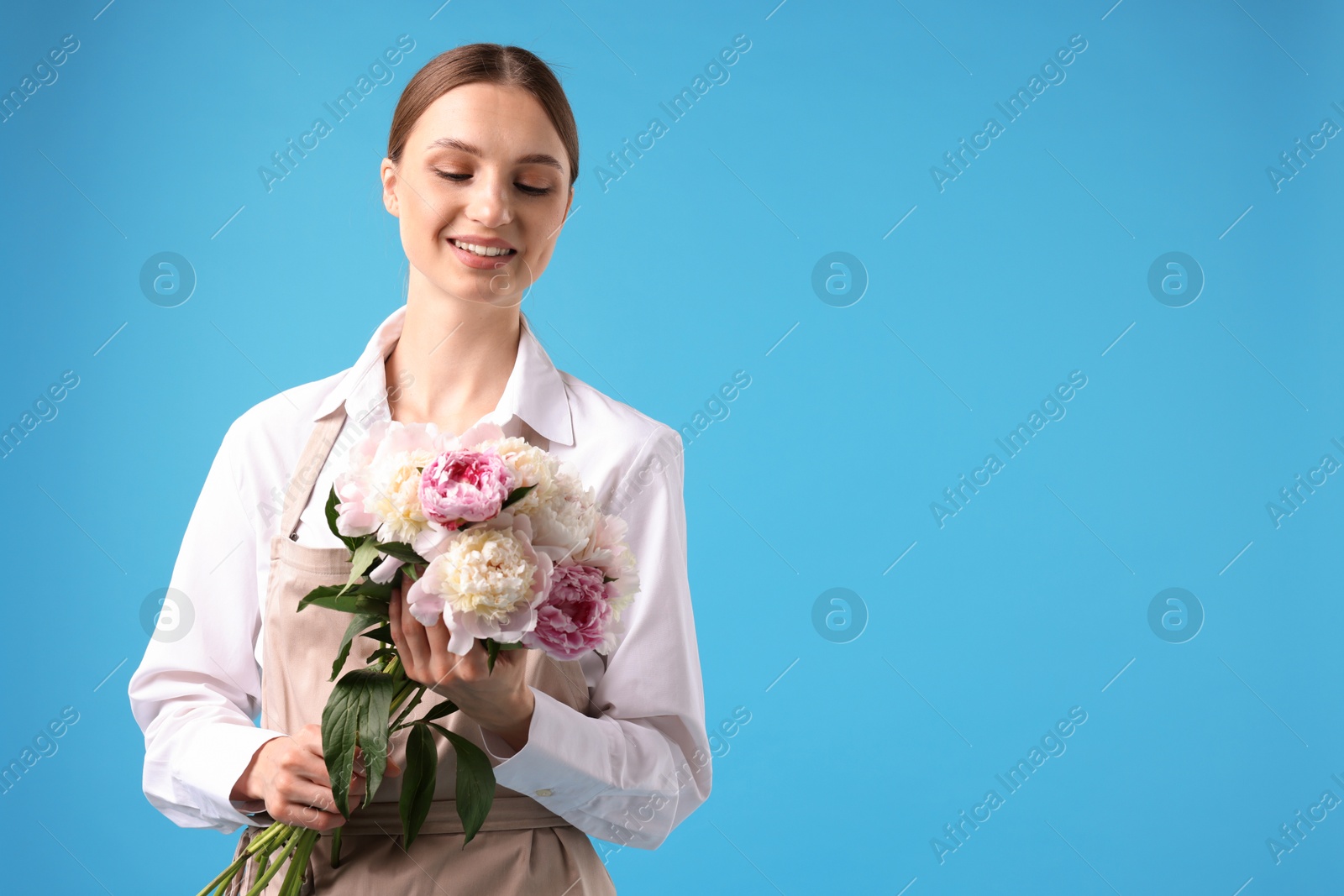 Florist with beautiful bouquet of peonies on light blue background, space for text Photo of Florist with beautiful bouquet of peonies on light blue background, space for text