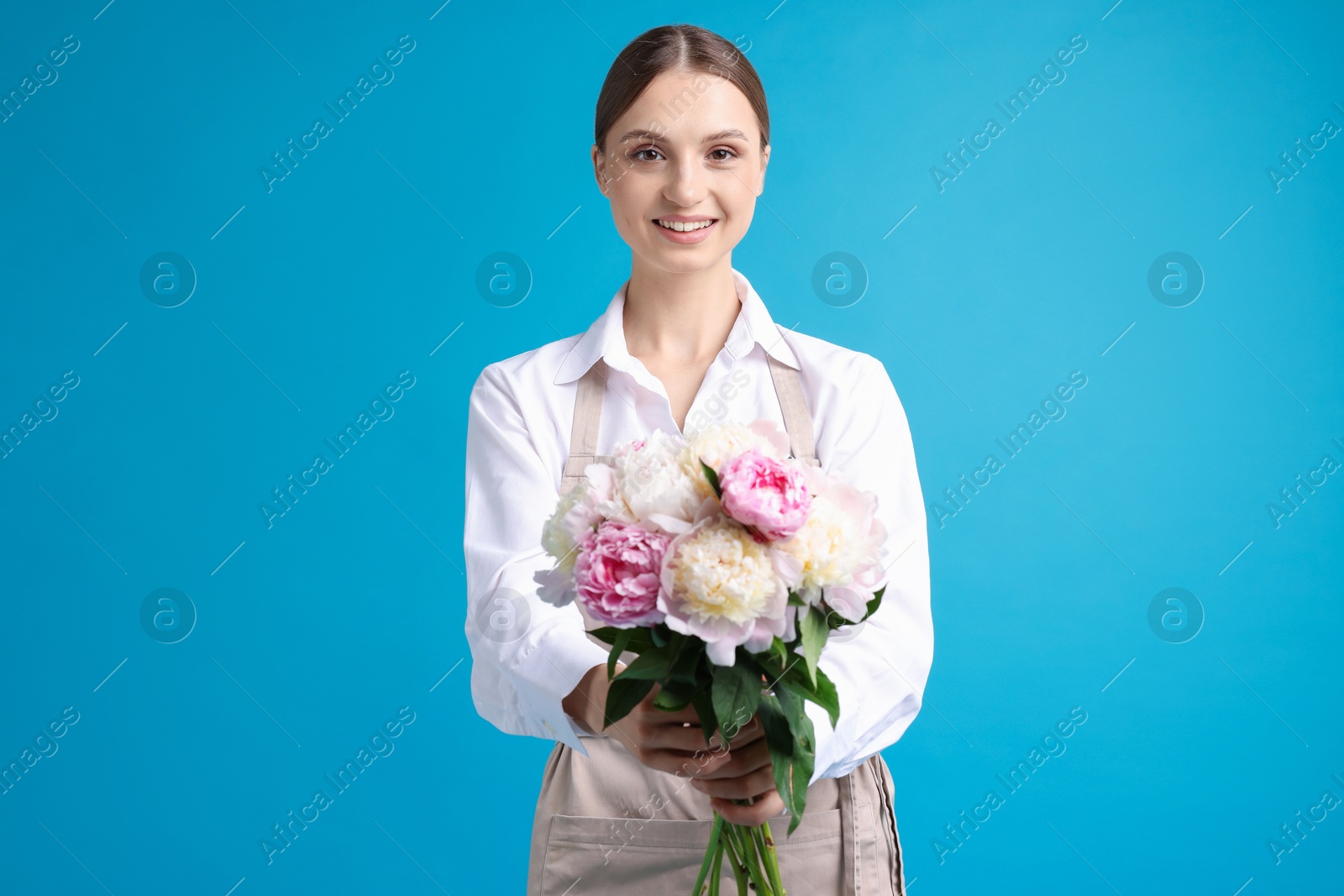 Florist with beautiful bouquet of peonies on light blue background Photo of Florist with beautiful bouquet of peonies on light blue background
