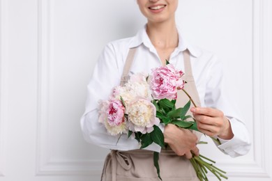 Photo of Florist with beautiful bouquet of peonies near white wall indoors, closeup. Space for text